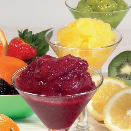 Trio farebných sorbetov servírovaných v priehľadných pohároch, obklopených čerstvým ovocím vrátane jahôd, pomarančov a kiwi, zdôrazňujúce bohatú chuťovú paletu a sviežosť ponuky.